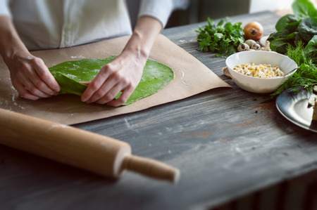 chef rolls the dough for ravioli with spinach adding to the dough, stuffed with porcini mushrooms and ricotta. with quail eggs poached. on a dark background.の写真素材