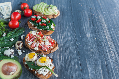 tasty and delicious bruschetta with tomatoes, spinach, feta avocado red chili pepper and blue cheese. With Micro Green and sesame seeds and flax. healthy eating concept.の写真素材
