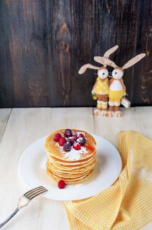 Pancake on a white plate with fruit and powdered sugar on a wooden backgroundの写真素材