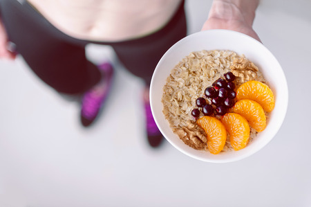 Oatmeal with fruit berries and cereals in the hands of a sportswomanの写真素材