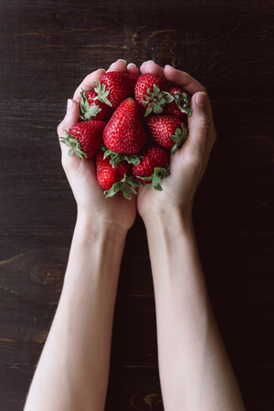 Ripe organic strawberries in hands on a rustic wooden rustic backgroundの写真素材