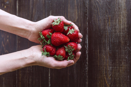 Ripe organic strawberries in hands on a rustic wooden rustic backgroundの写真素材