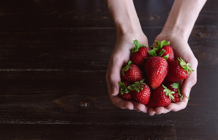 Ripe organic strawberries in hands on a rustic wooden rustic backgroundの写真素材