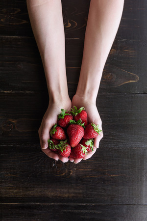 Ripe organic strawberries in hands on a rustic wooden rustic backgroundの写真素材
