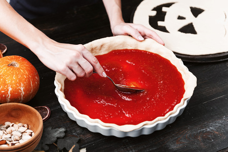 Chef cooks a pie for Halloween with a filling of pumpkin-strawberry jam and peachesの写真素材