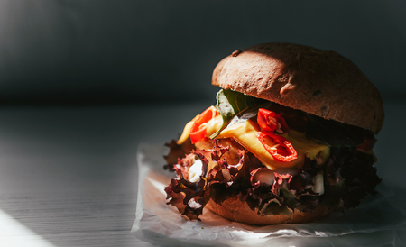 Delicious and appetizing burger with chicken cutlet, basil and chili pepper on a white wooden backgroundの写真素材