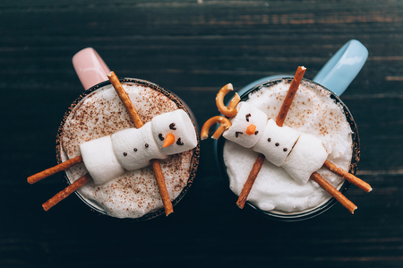 a mug with hot chocolate on a wooden table with a marshmallow man who is resting in a mugの写真素材