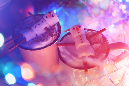 a mug with hot chocolate on a wooden table with a marshmallow man who is resting in a mugの写真素材