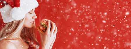 girl in red dress and santa hat with burger in handsの写真素材