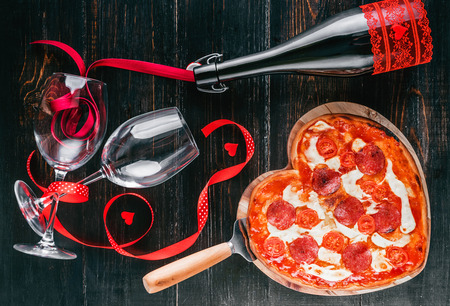 a festive dinner of pizza in the shape of a heart and a bottle of wine.の写真素材