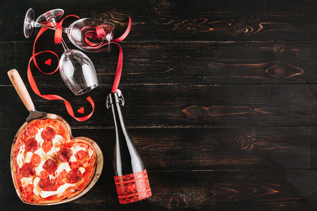 a festive dinner of pizza in the shape of a heart and a bottle of wine.の写真素材