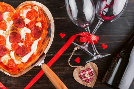 a festive dinner of pizza in the shape of a heart and a bottle of wine.の写真素材