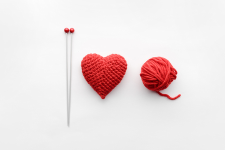 a knitted heart of red thread with an inserted knitting needle on a white background. and a hank of a red knitting threadの写真素材