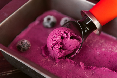 pink ice cream with a spatula for ice cream on a dark wooden background with waffle cupsの写真素材
