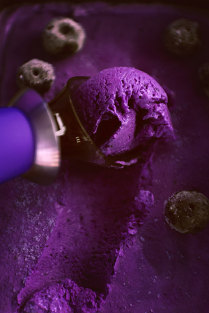 Purple ice cream with a spatula for ice cream on a dark wooden background with waffle cupsの写真素材