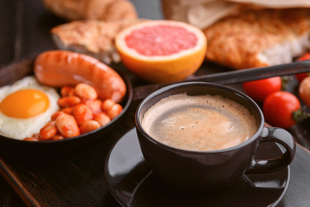 English breakfast. sausage, fried eggs and beans in tomato. coffee and bread nearby.の写真素材