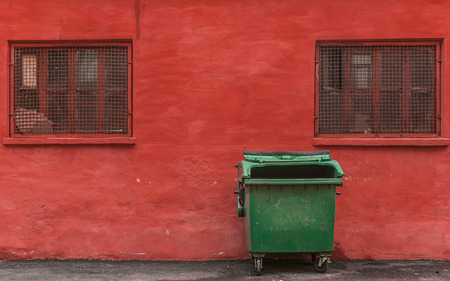 green garbage container on a red wall backgroundの写真素材