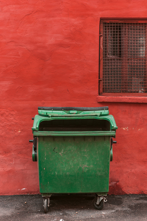 green garbage container on a red wall backgroundの写真素材