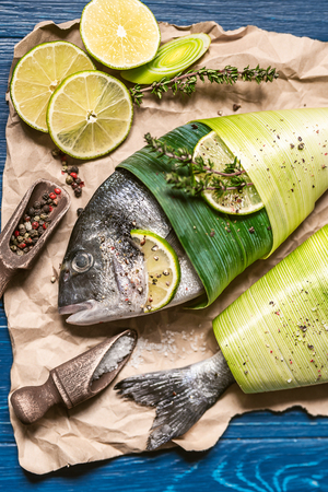 two fresh raw dorado fish, wrapped in palm leaves, sprinkled with a mixture of peppers and large gimolais salt, with slices of lime and lemon, ready to be baked. cooking dinner concept for twoの写真素材