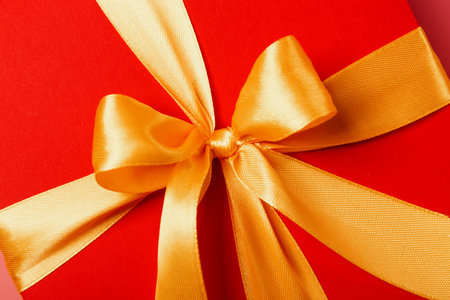 red box tied with a gold ribbon. the ribbon is tied on a box in the form of a beautiful bow. holiday...