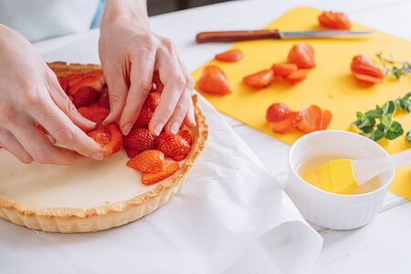 ingredients for strawberry pie, custard cake with lime zest, cutting board with sliced strawberries. female hands lay sliced strawberries on the surface of the creamの写真素材