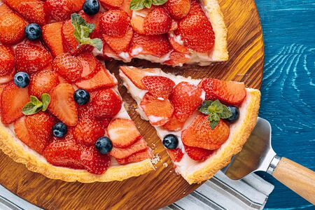 quiche with lime zest and strawberry slices with blueberries and fresh mint leaves on a blue wooden table. one slice is cut out of the pie and it is ready to serve.の写真素材
