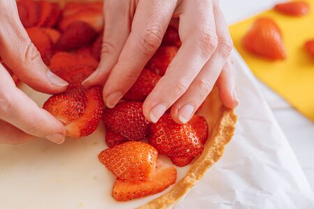 ingredients for strawberry pie, custard cake with lime zest, cutting board with sliced strawberries. female hands lay sliced strawberries on the surface of the creamの写真素材
