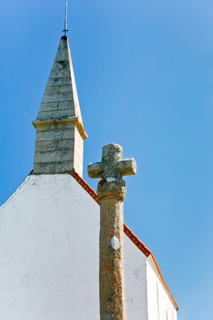 old stone cross and roof of country Chapelle Saint Michel with blue sky backgroundの写真素材