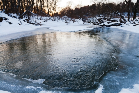 frozen banks of forest pond at winter sunsetの写真素材