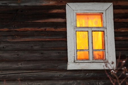 bright yellow lighting window of rural log house in winterの写真素材