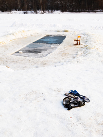 slippers and chair near ice hole in frozen lake in cold winter dayの写真素材