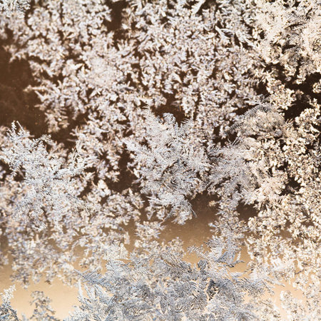 snowflakes and frost on glass close up - frosty brown white pattern on window in cold winter day