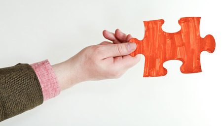 red painted puzzle piece in male hand on grey backgroundの写真素材