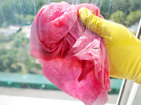 hand in yellow rubber glove cleaning window glass by wet cloth
