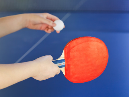 girl plays in table tennis with red racket on blue tenis table close upの写真素材