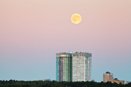 full moon in pink sky over urban houses in summer eveningの写真素材
