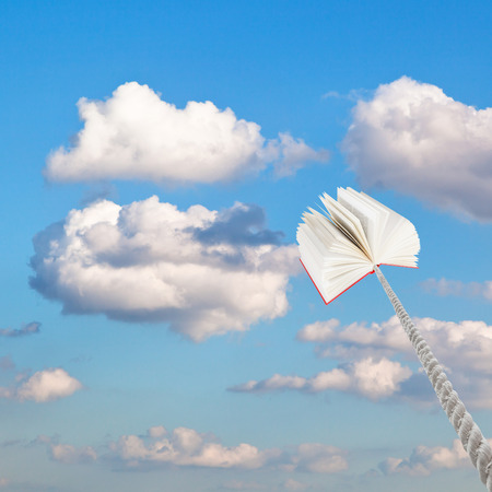 book tied on rope soars into sky with little white cloudsの写真素材