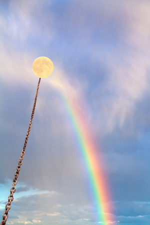 yellow full moon tied on chain soars into sky with rainbowの写真素材