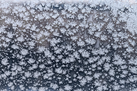 snowflakes and frost on frozen windowpane in cold winter evening close up