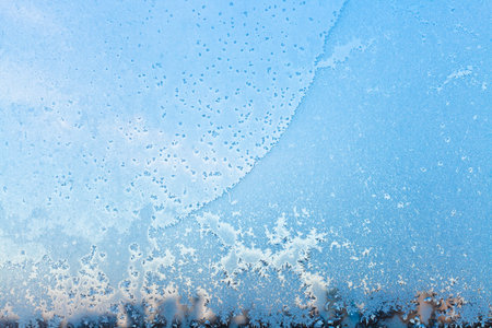 window pane with snowflakes and frost pattern in cold winter day