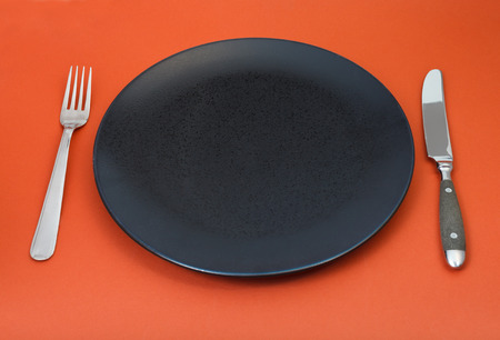 empty black plate with fork and knife on red backgroundの写真素材