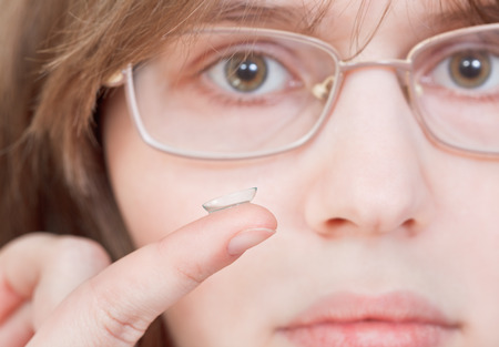 girl with glasses holds contact lens on your finger near the eyesの写真素材