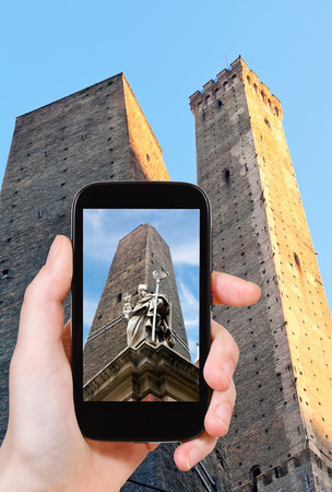 travel concept - tourist taking photo of saint petronius statue and two tower in Bologna on mobile gadget, Italyの素材 [FY31037291105]