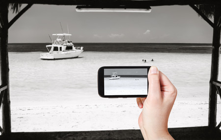 travel concept - tourist taking photo of yacht in Atlantic Ocean on mobile gadget, Varadero, Cubaの写真素材