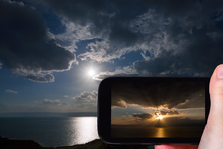 travel concept - tourist taking photo of sunset on Dead Sea on mobile gadget, Jordan