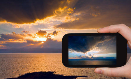 travel concept - tourist taking photo of sundown on Dead Sea on mobile phone, Jordan