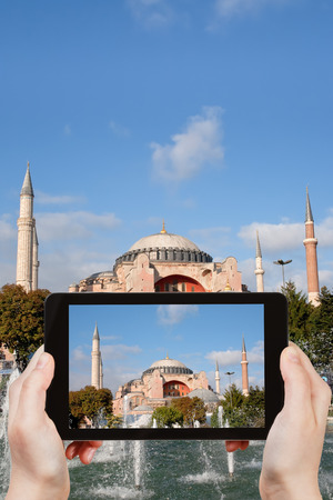 travel concept - tourist taking photo of Haghia Sophia through fountain on Sultanahmet square on mobile gadget, Istanbul, Turkeyの写真素材