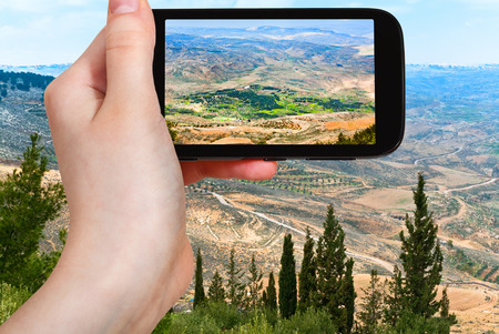 travel concept - tourist taking photo of Holy Land from Mount Nebo in Jordan on mobile gadgetの写真素材