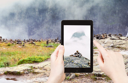 travel concept - tourist taking photo of stone pyramid on mountain plateau in Norway on mobile gadgetの写真素材