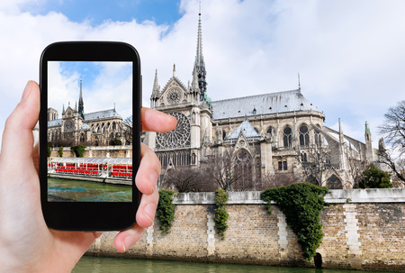 travel concept - tourist taking photo of cathedral Notre Dame de Paris and tourist boat on Seine River on mobile gadget, Franceの写真素材